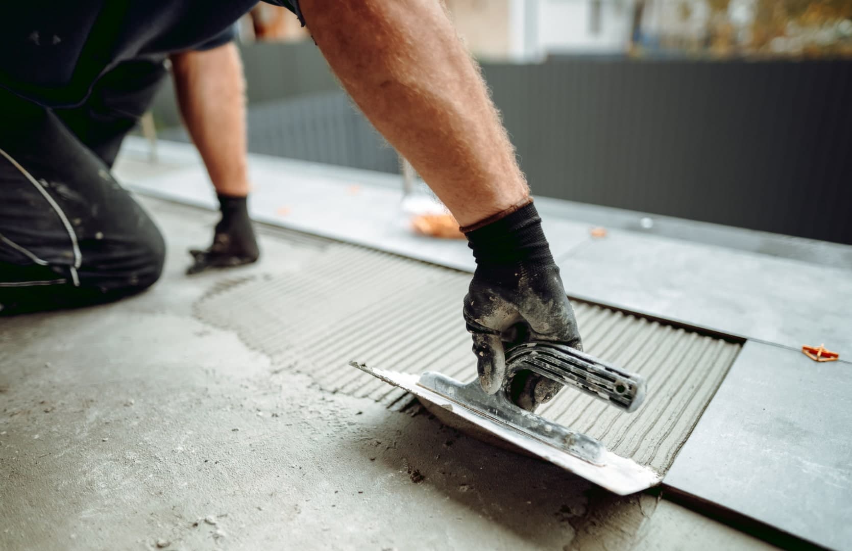Tiler spreading tile adhesive with a notched trowel before laying a floor tile